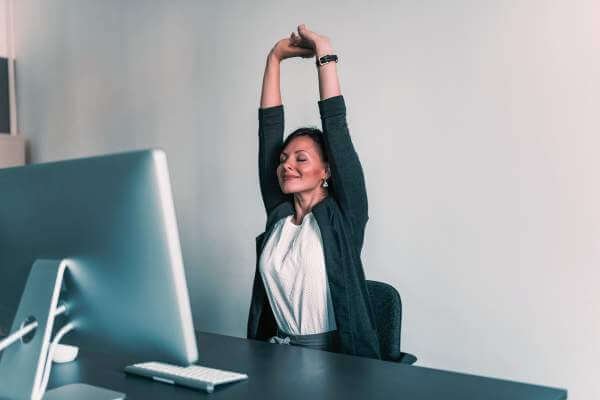 Pessoa fazendo alongamento na cadeira durante o expediente, aliviando tensões do trabalho sentado