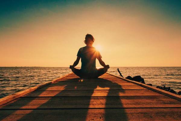 Pessoa sentada meditando com olhos fechados em um ambiente calmo, praticando mindfulness para estresse.