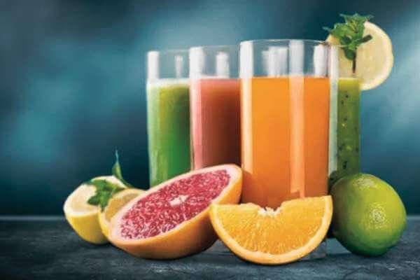 Sucos naturais variados em copos de vidro sobre uma mesa com frutas frescas.
